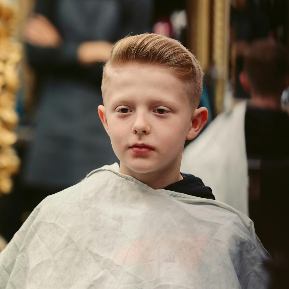 Un băiat cu o tunsoare modernă pentru băieți stă &icirc;ntr-un salon de coafură