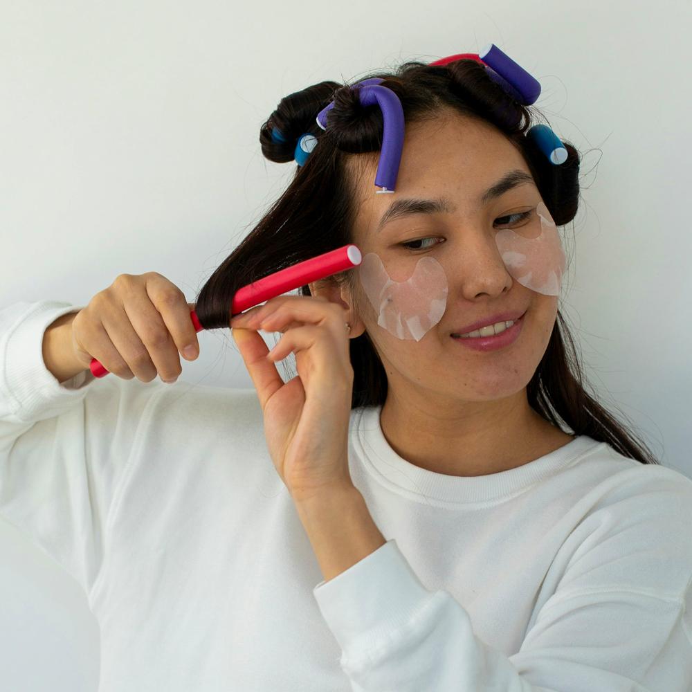 Femeie care &icirc;și pune bigudiuri pe păr &icirc;n timpul coafării acasă